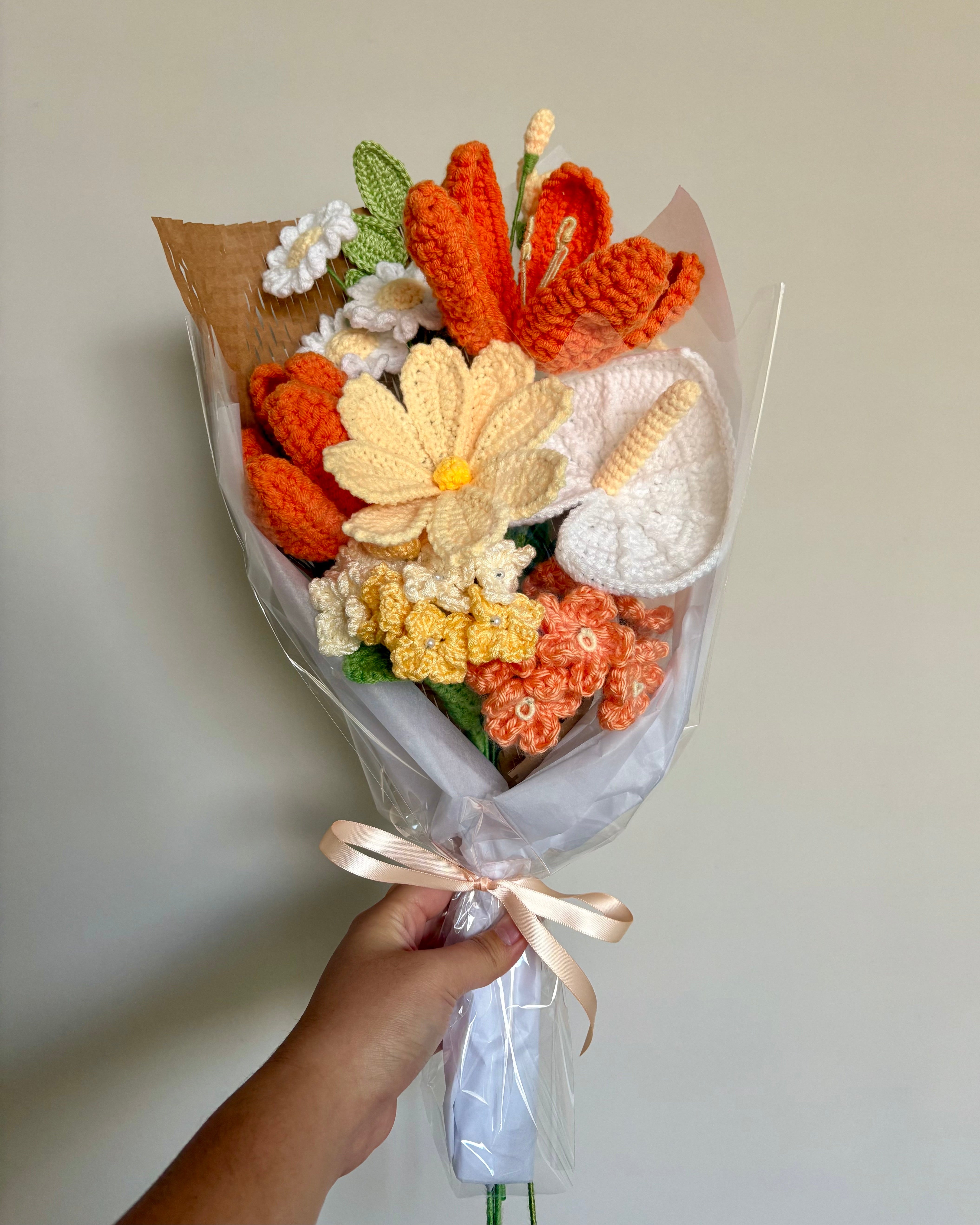 Bouquet of crocheted flowers in orange, yellow, and white held by a hand against a plain background