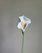 crocheted white calla lily flower with green stem on a plain background